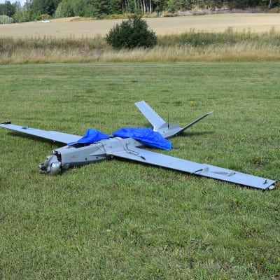 En drönare på gräset. Drönaren är av modellen som ser ut som ett litet flygplan. Den har skadats vid landningen.