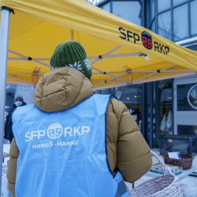 RKP:n liiviin pukeutunut henkilö RKP:n vaaliteltan edessä. Selässä lukee SFP RKP Hangö Hanko.
