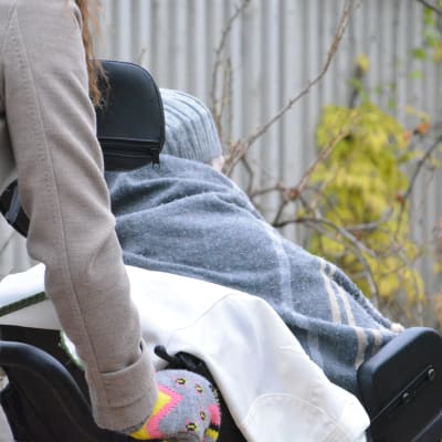 Kvinna skjuter på rullstol där det sitter en äldre person.
