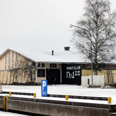 En gul gammal magasinbyggnad i Ekenäs norra hamn. På ena sidan syns en björk. Marken är täckt av snö.