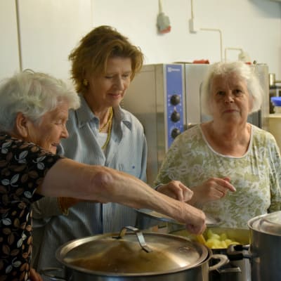 Ella Engberg, Loa Droz och Else-Maj Bäckström står i ett kök och rör i en kastrull med potatis.