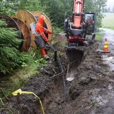 En grävmaskin gräver ett dike där det sätts ner jordkablar, luftkablarna tas alltså bort.