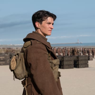 Tommy /Fionn Whitehead) står på stranden och i bakgrunden syns en massa andra soldater. 