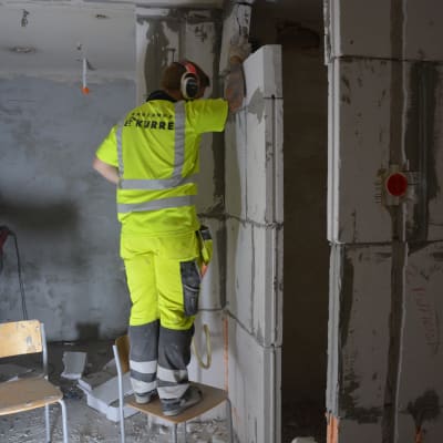 Byggarbetare står på en stol och murar en vägg.