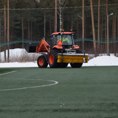 En traktor kör bort snö från sidorna av den uppvärmda konstgräsplanen i Karis den 6 mars 2018.