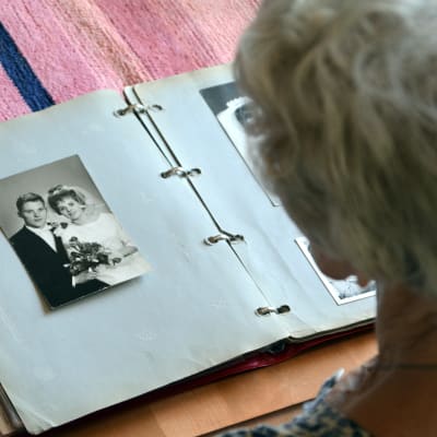 Gammal kvinna ser på ett gammalt bröllopsfoto i ett fotoalbum