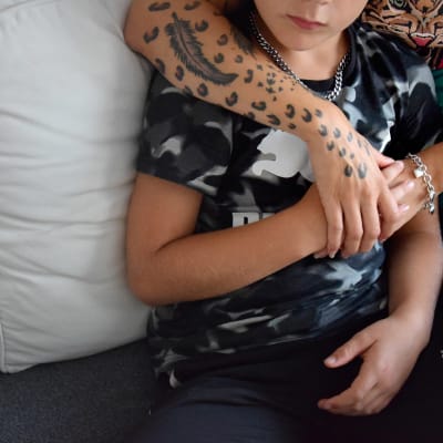 En bild på en arm med tatueringar som håller om en pojke. Pojken håller om handen.