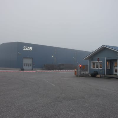 En fabrik i dimmigt septemberväder. Framför byggnaden en röd-vit bom  och ett rött trafikljus.