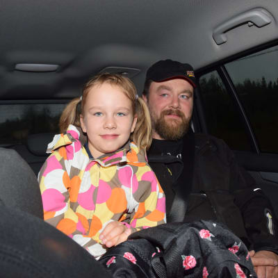 ett barn, flicka och en vuxen man (pappan) sitter i baksätet i en personbil.