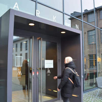 En kvinna med ljust hår sträcker sig mot en dörr in till Åbo Akademis hus Arken i Åbo.