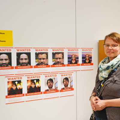 En kvinna står framför en vägg med bilder på misstänkta personer.