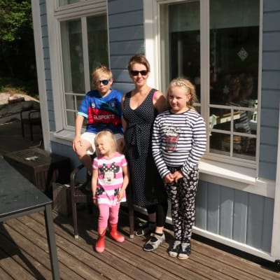Rosa Pentikäinen-Mattila står med sina barn i solskenet ute på terassen och tittar mot kameran.