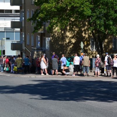 Ett femtiotal personer står i kö längs trottoaren.
