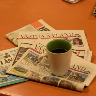 En kaffekopp och en hög med dagstidningar.