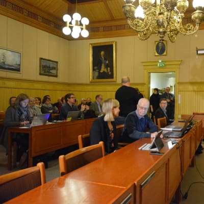 Fullmäktigeledamöter och medierepresentanter förbereder sig fusionsbeslut i Kaskö fullmäktigesal.