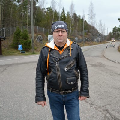 En man iklädd svartskinnjacka står på en väg. 