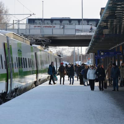 Vasa järnvägsstation, på spåret står ett vitt och grönt VR-tåg. På perongen finns många människor. Det är vinter och det ligger snö på marken.
