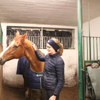 Lia Lundström och hennes häst i ett stall. Hästen nosar på en annan häst.