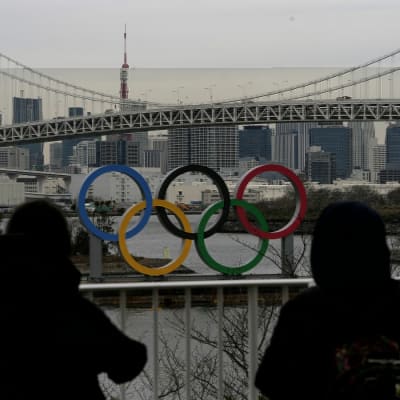 Två personer står och tittar på de olympiska ringarna i Tokyo