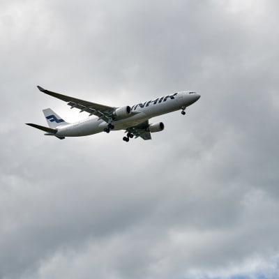 Finnairs flygplan flyger i en grå och molnig himmel.