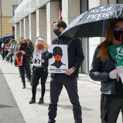 Szczecin kaupungissa kasvosuojiin pukeutuneet mielenosoittajat vastustavat lakialoitteita jonottamalla kaupan edustalla 14. huhtikuuta 2020. Jonottamalla he eivät riko koronaviruksen takia asetettua kokoontumisrajoitusta.