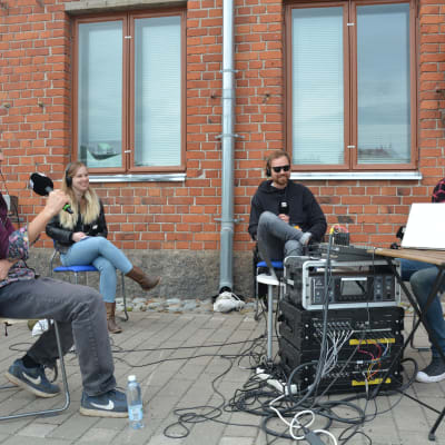 Kulturjournalisten Tomas Jansson, Viper Arms basist Soffe, Sivujuttus sångare Martin Laine och redaktören Joakim Rundt sitter på stolar framför en tegelvägg i en direktsändning om rockmusiken i Åbo.