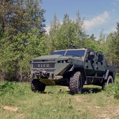 Ett militärfordon av modellen SISU GTP 4x4 står i mitten av bilden, runtom gräs och skog. 