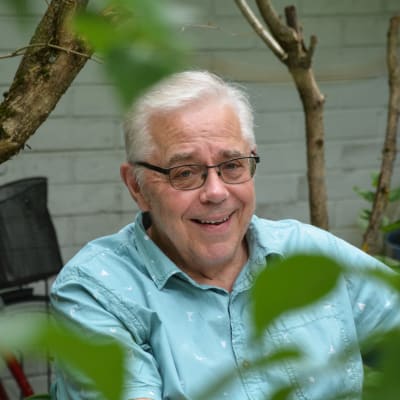 Egil Green sitter vid ett trädgårdsbord. Han ler och tittar in i kameran.