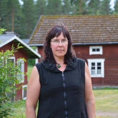 Katarina Rosas står ute på gården framför rödmyllade hus