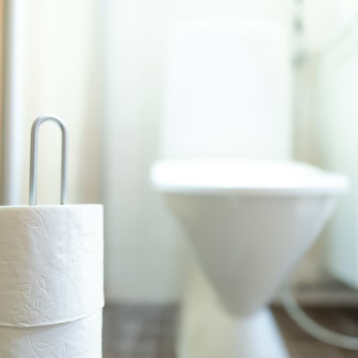 Toalettpapper i en ställning. I bakgrunden en wc-stol.