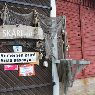 En dörr till en gammal träbyggnad som är inramad av fiskenät och med en skylt som säger 'Skärimuseum sista säsongen'.