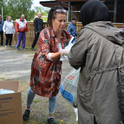 Muslimsk kvinna får munskydd av frivilligarbetare i brödkö.