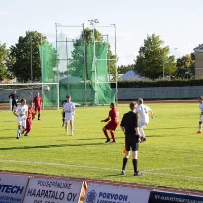 Fotbollsmatch på gräsplan. Ena laget spelar i vita tröjor, det andra i röda.