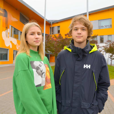 En flicka och en pojke framför en skolbyggnad.