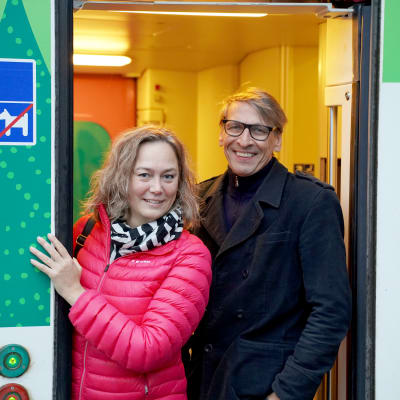 En glad man och en glad kvinna i en dörr till ett tåg.