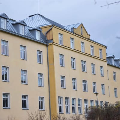 Ett stort rappat, gult hus i fyra våningar. Gammalt sjukhus.