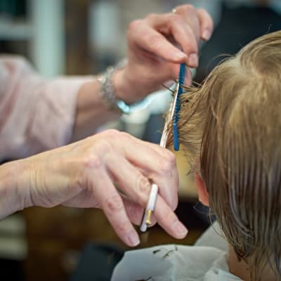 Nuori poika parturi-kampaajalla leikkauttamassa hiuksiaan.