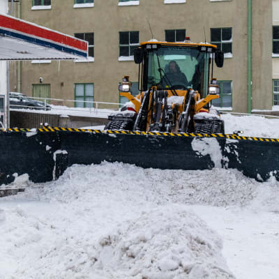 Traktor röjer snö på gård.