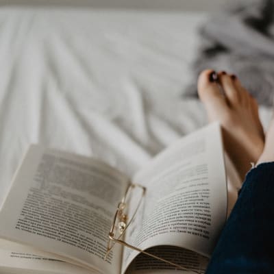 Någon läser en bok i sängen med glasögonen liggande i boken.