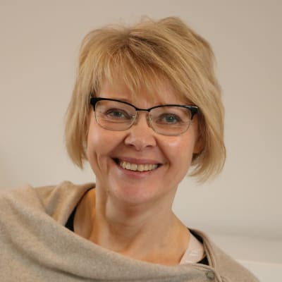 En kvinna med kort blont hår och glasögon skrattar.