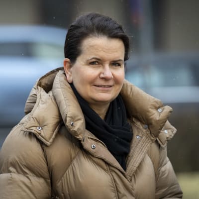 HUS biträdande överläkare Eeva Ruotsalainen står ute i en beige dunjacka. Bakom henne syns bilar parkerade.
