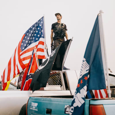 En man omgiven av flaggor står på flaket till en pick-up