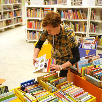 En bibliotekarie radar böcker i en låg låda på bibliotekets barnavdelning.
