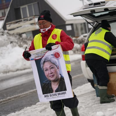 Henkilö kantaa vaalijulistetta, taustalla toinen nostaa julisteita auton peräkontista