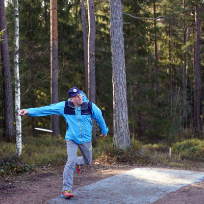 En man kastar fribeegolf. Han tar sats och står egentligen bara på ett ben.