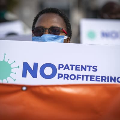 En demonstrant håller upp ett plaket med texten "No Patents profiteering"