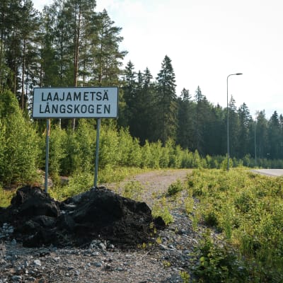 En asfalterad väg i en skog och en skylt där det står Laajametsä/Långskogen.