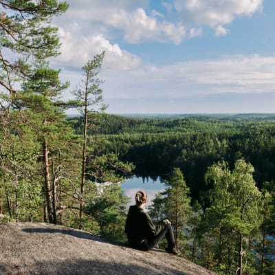 Nainen istuu kallioilla ja katsoo kohti järveä. 