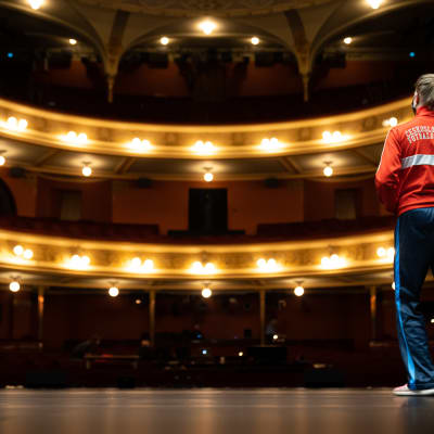 Auri Ahola fotograferad bakifrån på scenen i Nationalteatern framför tomma läktare..