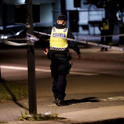 Poliisi kävelee keltaisessa liivissä selin pimeässä illassa paikassa, jossa hänen poliisikollegansa ammuttiin. 